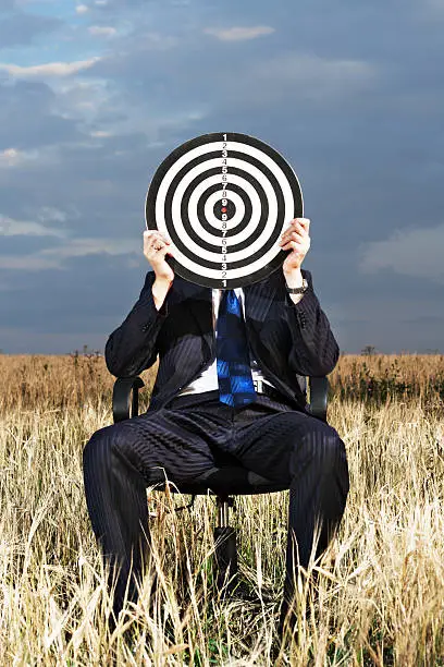 Photo of A man sitting down holding a target board up to his face