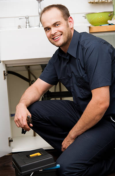 A kneeling male plumber poses happily next to a kitchen sink stock photo