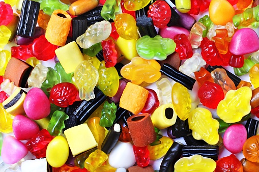 Photograph of colorful sugar coated gumdrops, jellybeans, jujuba or jujubes in a glass bowl isolated against plain, white background shot from top. A hot favorite with kids and some grownups too.