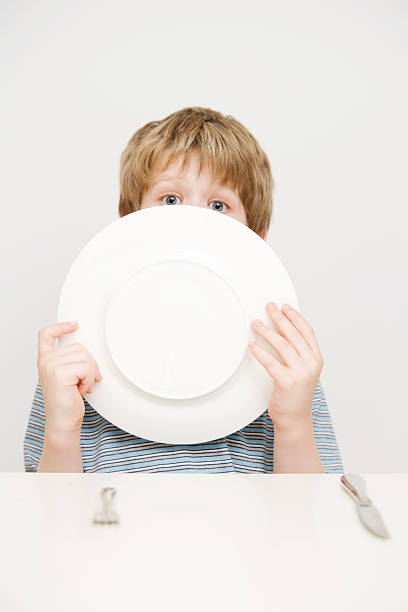 Child Boy with Knife and Fork Licking  Dinner Plate stock photo