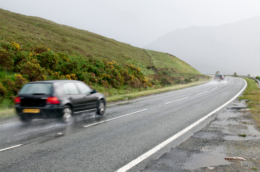 Two cars speed along a winding wet country road in Scotland.