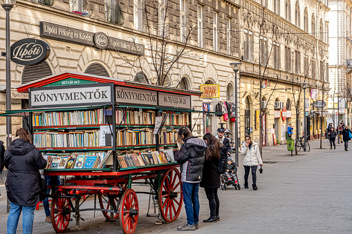 Budapest, Hungary - 04 March 2023:Mobile book cart in Budapest. Traditional antique bookstore in the center of the city. Buyers choosing and reading books.