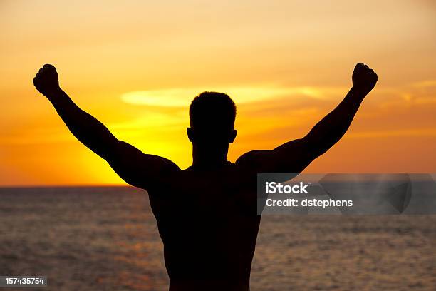 Muscular Man Silhouetted Contra La Puesta De Sol Foto de stock y más banco de imágenes de Adulto - Adulto, Alzar los brazos, Anochecer