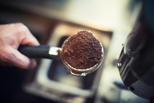 A barista holds a freshly ground  shot filter of coffee beans, ready to be made into an espresso.  Very shallow depth of field, horizontal with copy space. 