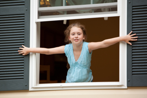 Little girl looking from the open window of country house