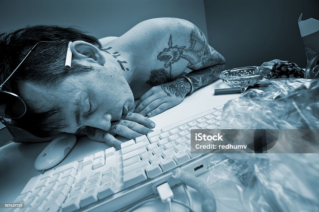 Man sleeping at the computer A stock photo of a topless man with cigarette and sunglasses who has fallen asleep at the computer exhausted and sleep deprived surrounded by junk food remnants and wrappers. Computer Stock Photo