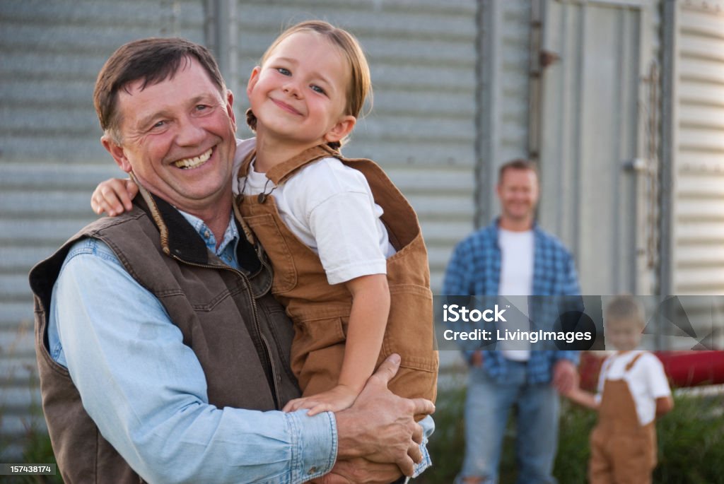 Family Farm Grandfather in front of a grain bin holding his granddaughter, son and grandson are in the background. Family Stock Photo