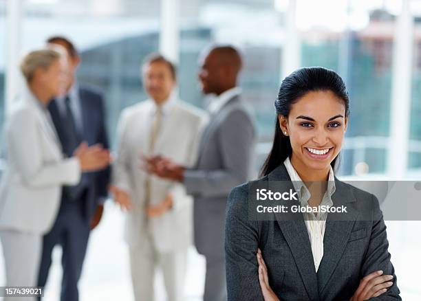 Geschäftsfrau Lächelnd Mit Kollegen Im Hintergrund Stockfoto und mehr Bilder von 20-24 Jahre - 20-24 Jahre, Anzug, Arbeitskollege
