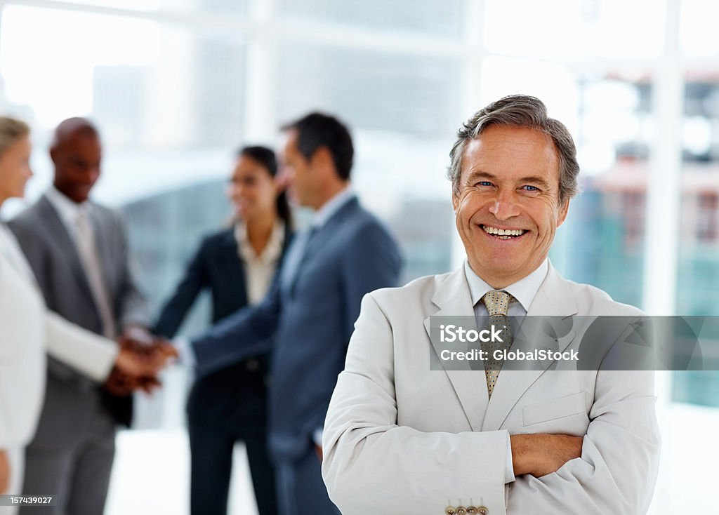 Бизнесмен, улыбается с коллегами в фоновом режиме - Стоковые фото 50-54 года роялти-фри
