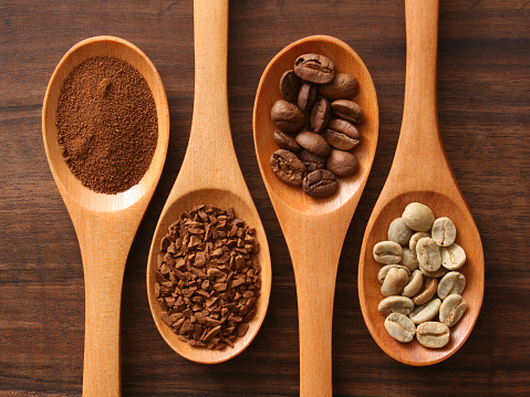 Instant coffee and grains over spoons (powdered, granulated, beans, raw beans)