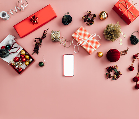 A from above view of a smartphone being used for buying beautiful New Year presents. (studio shot, pink background, e-banking concept)