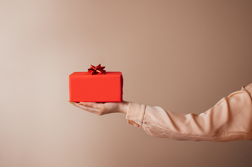 Giving is receiving: A side view of an unrecognizable Caucasian woman holding a beautiful Christmas present. (studio shot, white background, cropped photo)