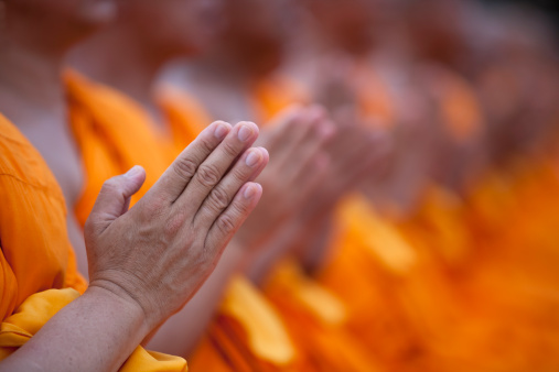 Buddhist monks paying respect to the Lord Buddha at a Buddhist temple in Thailand, with a traditional hand gesture. Very shallow depth of field with the focus being on the hands in the foreground. 