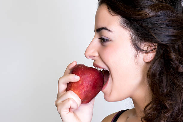 Brunette woman biting into a red apple stock photo