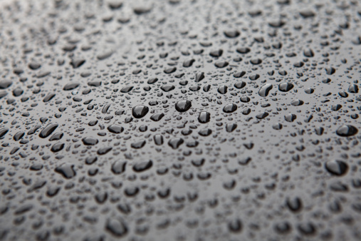 closeup of raindrops on a black vehicle (this one happens to be a motorcycle tank)