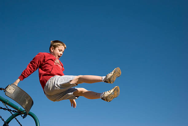 Boy Jumping Off Swing With Clear Blue Sky stock photo