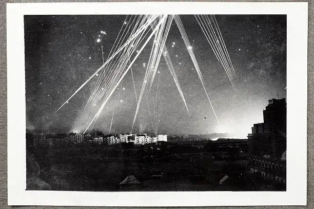 Rare black and white wartime photograph of a night air raid on Alexandria, Egypt in 1943. Anti-aircraft tracer bullets light up the sky and a series of explosions illuminate the right hand horizon. Dust and scratches reflect age and condition of original image.