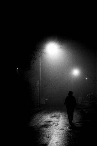 Lost man walking in dark foggy street towards illuminated balloon.