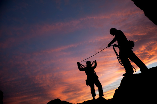 Two mountain climbers coil their rope after a climb at dusk