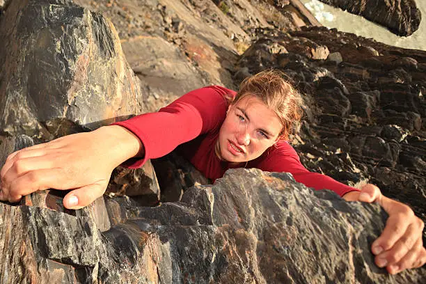 A view directly above a young woman climbing a rock face. She is determined to succeed.