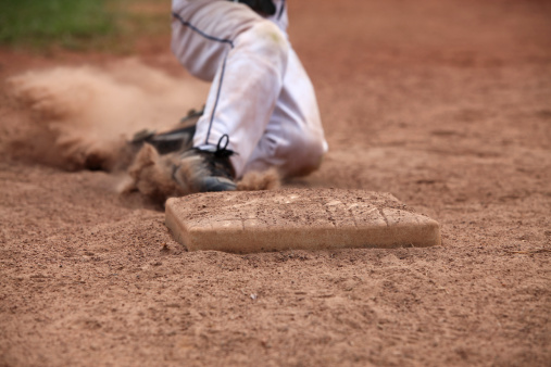 Third baseman ready to tag out the arm of a sliding runner during a baseball game