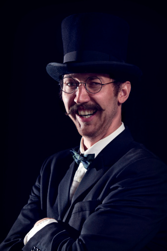 A sophisticated and classy looking man in a top hat and spectacles poses for a portrait.  Vertical with copy space.  Handle bar mustache is 100% real.
