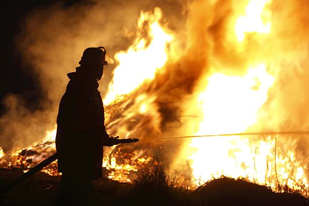 firefighter holding hose pointing water stream onto fire - orman yangını stok fotoğraflar ve resimler