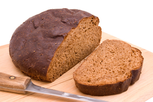 Loaf of freshly baked dark bread on a blackboard a white wooden background