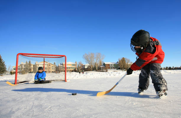 joven caucásico niños jugando hockey sobre hielo en pista al aire libre. - slap shot fotografías e imágenes de stock