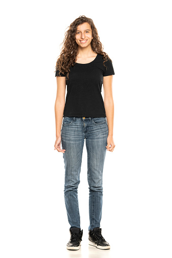 Full length shot of smiling young woman wearing black shirt and blue jeansi while standing at isolated white studio background.