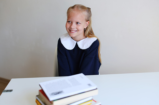 Photo of sweet charming schoolgirl smiling sitting white table