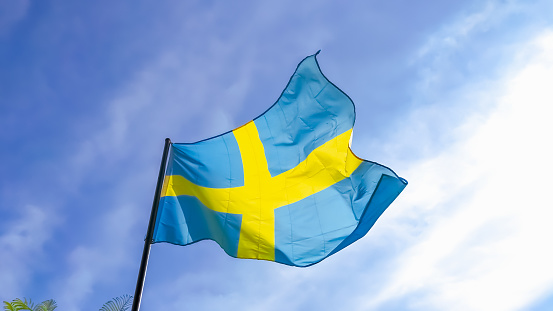 Low angle view of Sweden National Flag waving in the wind under cloudy blue sky