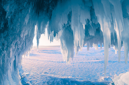 Ice cave with icicles on Baikal lake at sunset. Winter landscape of Baikal lake, Siberia, Russia