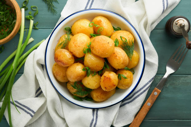 istock Fresh boiled new or young potatoes with butter, fresh dill and onions in white bowl on old rustic wooden background. Tasty new boiled potatoes. Top view. 1574465293