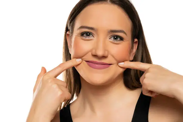 Photo of Young woman forcing her smile with her fingers on white background