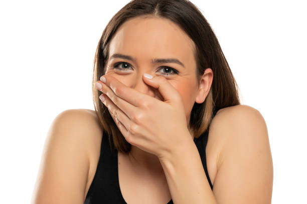mujer joven sonriendo y cubriéndose la cara con la mano - avergonzamiento fotografías e imágenes de stock