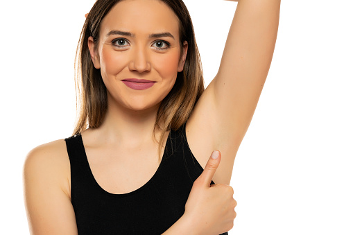 smiling young woman shows her shaved armpit and showing thumbs up on a white background.