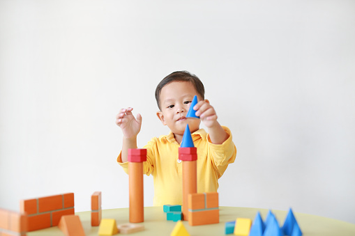Cheerful little baby boy playing a colorful wood block toy on table over white background.