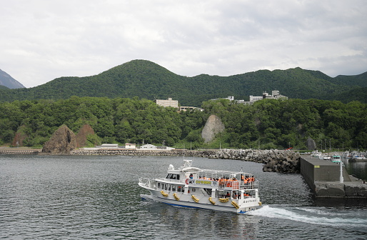 Shari District, Japan: Passengers fill a tour boat leaving Utoro Fishing Port for a cruise along the Shiretoko Peninsula. A popular hotel district stands on the hill at Utorokagawa. Spring afternoon in eastern Hokkaido Prefecture.