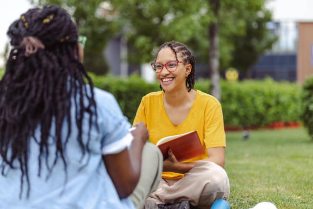 istock Two young African American female students sitting on the grass, studying and talking 1574559819