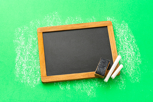 Chalkboard eraser and chalk pieces on green background. Copy space.
