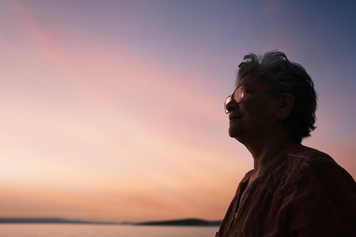 Silhouette of a smiling old woman with eyeglasses at sunset