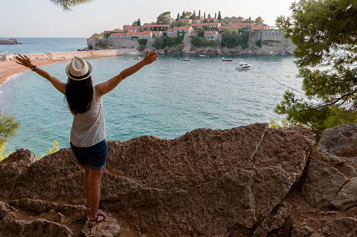 girl tourist in a hat looks from a cliff on the island of Sveti Stefan in Montenegro