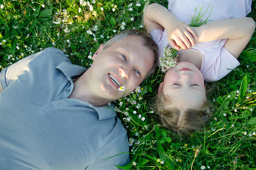 Daddy and daughter lying in a meadow with daisies. The girl is holding a bouquet of daisies.