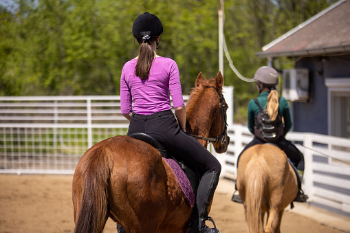 Two girls riding horses together outdoors on a ranch.