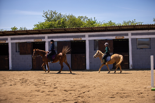 Two girls riding horses together outdoors on a ranch.