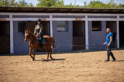 Woman having horseback riding lessons with instructor on a ranch outdoors.