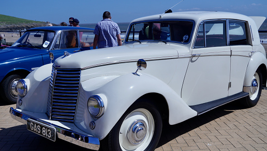 Barry Island, Vale of Glam, Wales - June 11 2023: Close up shot of the front of a stunning, white 1930's Armstrong Siddeley Special on display at a car show with chrome grill. headlamps and badge