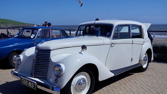 Barry Island, Vale of Glam, Wales - June 11 2023: Close up shot of the front of a stunning, white 1930's Armstrong Siddeley Special on display at a car show with chrome grill. headlamps and badge