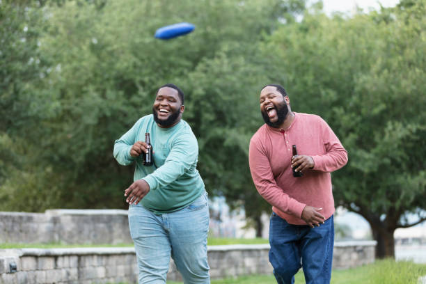 istock Two heavyset black men playing bean bag toss, drink beer 1574638382